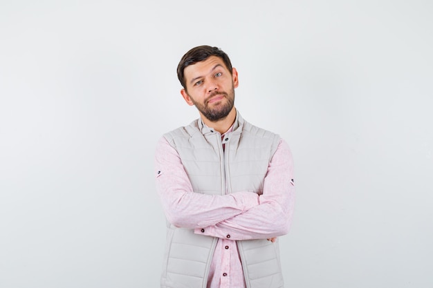 Portrait of elegant young man holding arms folded in shirt, vest and looking pensive 