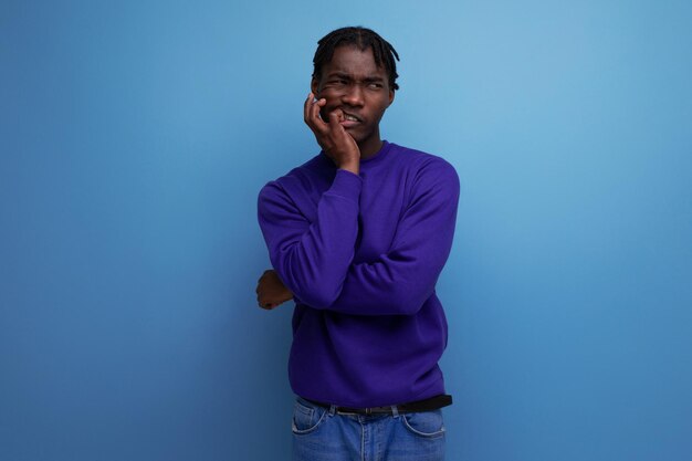 Portrait of an emotional darkskinned african young guy in a blue sweatshirt and jeans in the studio