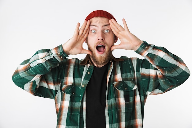 Portrait of emotional guy wearing hat and plaid shirt shouting, while standing isolated over white background