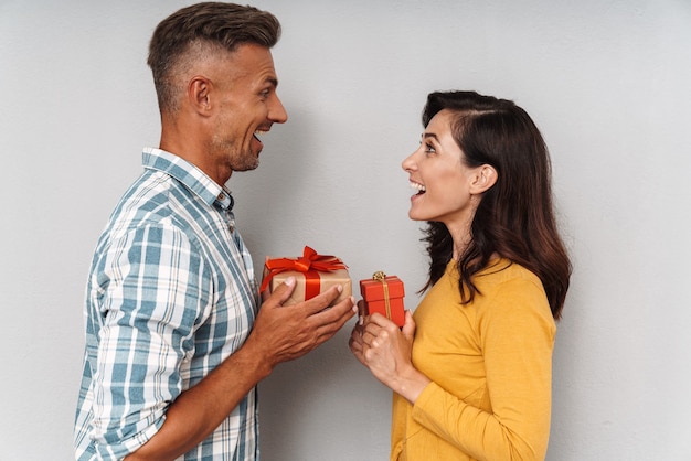 Portrait of a emotional shocked surprised cute optimistic adult loving couple isolated over grey wall holding gifts for each other