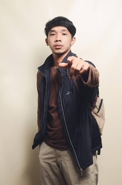 Portrait of energetic asian college young man wearing brown tshirt and black vest isolated on background