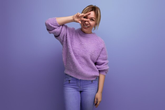 Portrait of an energetic bright blond young woman in a lavender sweater smiling at the camera