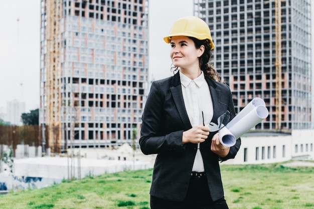 A portrait of engineer woman looking at construction. Woman architect with blueprint in hand and yellow helmet with select focus. Concept Engineer and business work.