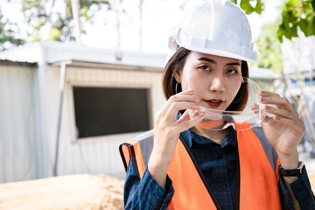 Portrait of engineer woman standing and take off the glasses\
after check project and statistical report on site. back view of\
contractor on background of modern home buildings with\
building.