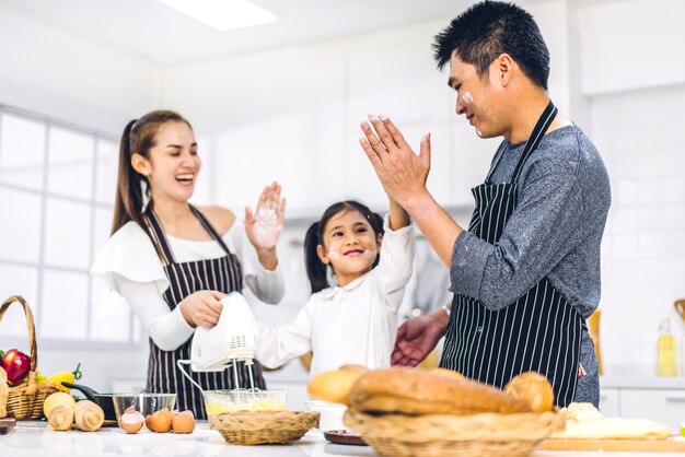 Portrait of enjoy happy love asian family father and mother with little asian girl daughter child having fun cooking together with baking cookies and cake ingredients on table in kitchen