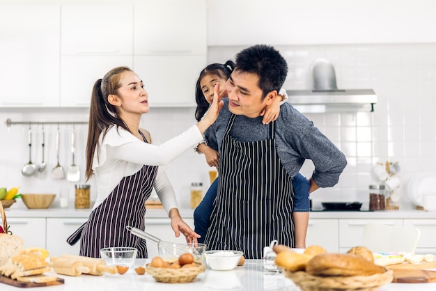 Portrait of enjoy happy love asian family father and mother with little asian girl daughter child play and having fun cooking food together with baking cookie and cake ingredient in kitchen