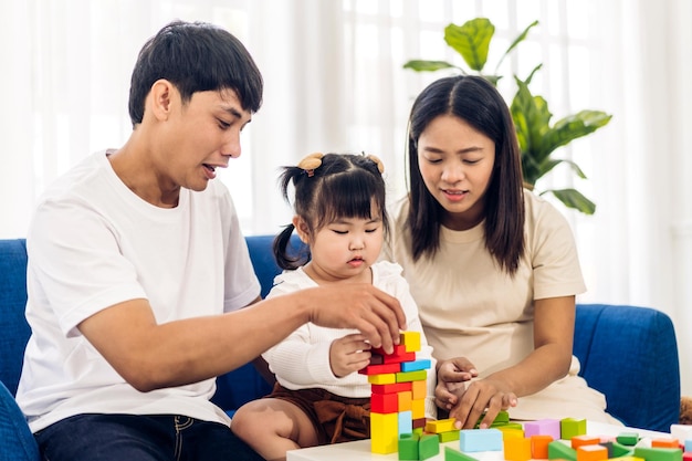 Portrait of enjoy happy love asian family father and mother with little asian girl smiling activity learn and skill brain training play with toy build wooden blocks board education game at home