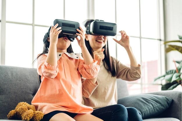 Portrait of enjoy happy love asian family mother and little asian girls child smiling and having fun using glasses of virtual reality headset.