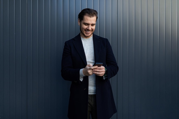 Portrait of a european smiling freelance man with a smartphone against the background of a building