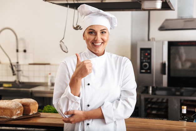 Portrait of european woman chef wearing white uniform, posing in kitchen at the restaurant
