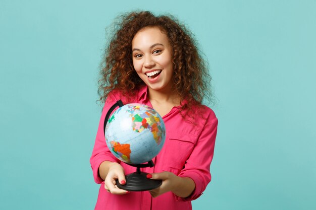 Portrait of excited african girl in casual clothes holding in hands Earth world globe isolated on blue turquoise background in studio. People sincere emotions, lifestyle concept. Mock up copy space.