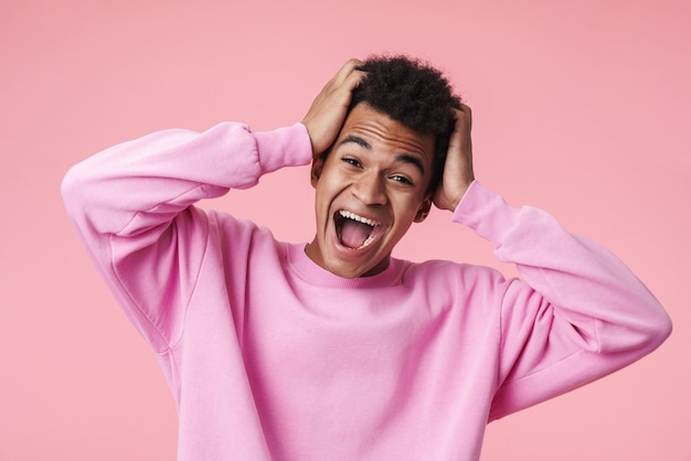 Portrait of an excited african teenager boy wearing pullower standing isolated on pink, screaming