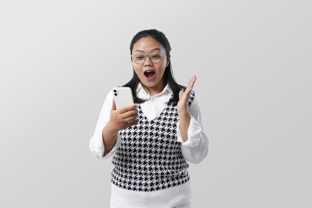 portrait of excited asian girl typing and holding phone isolated on white background