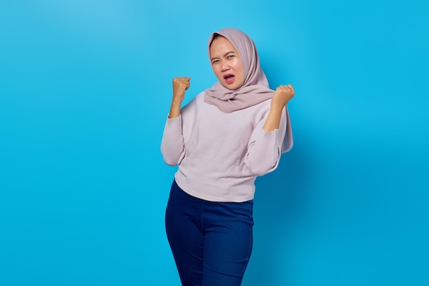 Portrait of excited asian woman celebrating success with raised arms