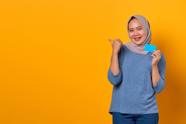 Portrait of excited Asian woman holding credit card and pointing finger at empty space