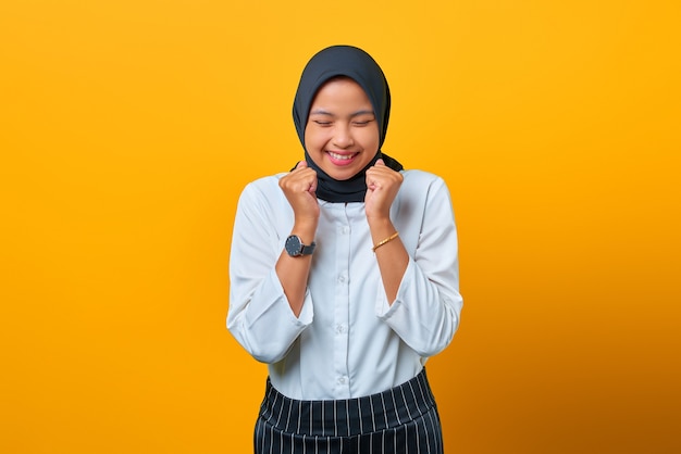 Portrait of excited beautiful Asian woman celebrating success on yellow background