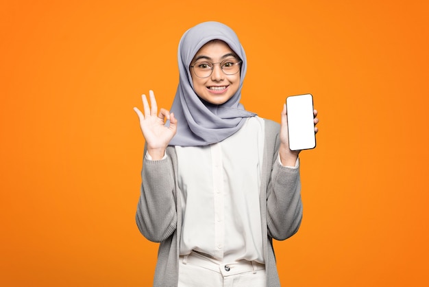 Photo portrait of excited beautiful asian woman showing okay sign and holding smartphone