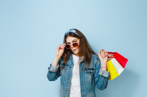 Portrait of an excited beautiful girl with sunglasses holding shopping bags isolated over blue background