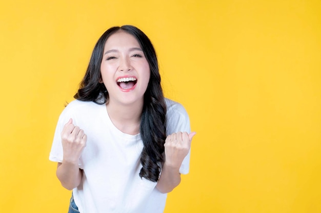 Portrait of excited beautiful happy Asian woman with happiness celebrating success isolated on yellow background