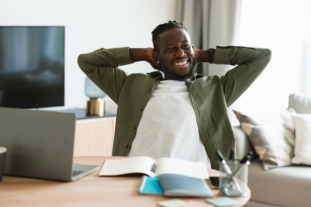 Portrait of excited black businessman relaxing on chair leaning\
back holding hands behind head and smiling