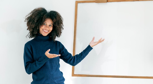 Portrait of excited black woman showing and pointing at blank white board presenting mock up background