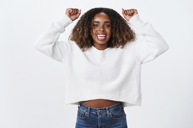 Ritratto eccitato affascinante donna afro-americana solidale alza le mani in alto allegria sorridente incoraggia ampiamente amico fan soddisfatto goal segnato, celebrando il successo della vittoria