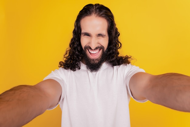 Portrait of excited cheerful guy take selfie toothy smile blink eye on yellow background