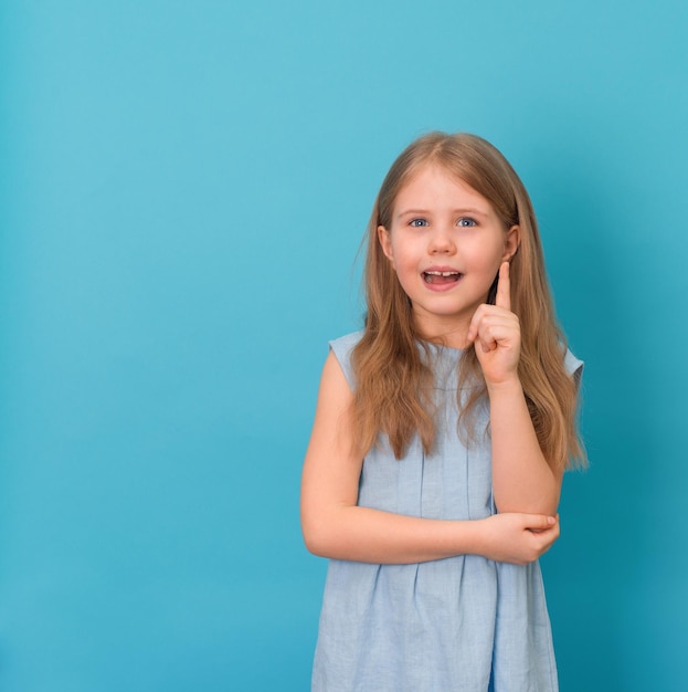 Portrait of a excited child pointing over blue background Little girl points finger up Copy space