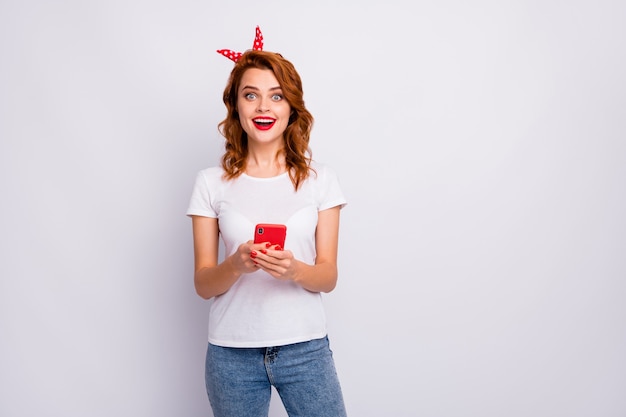 Portrait of excited crazy girl use smart phone read social media news impressed scream wow omg wear stylish clothing isolated over white color wall