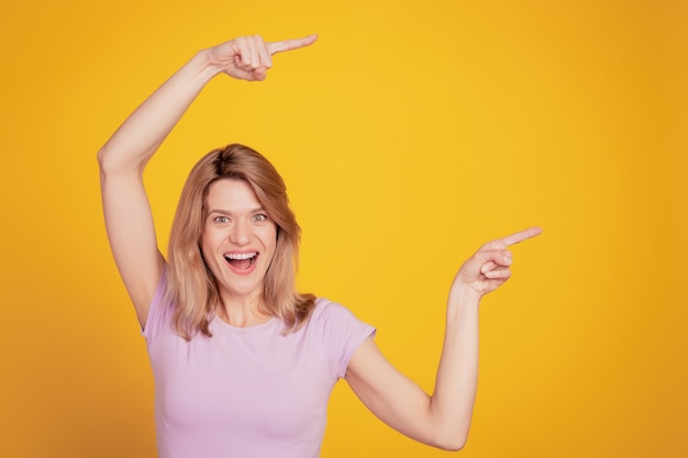 Portrait of excited funny promoter lady indicate forefingers blank space on yellow background