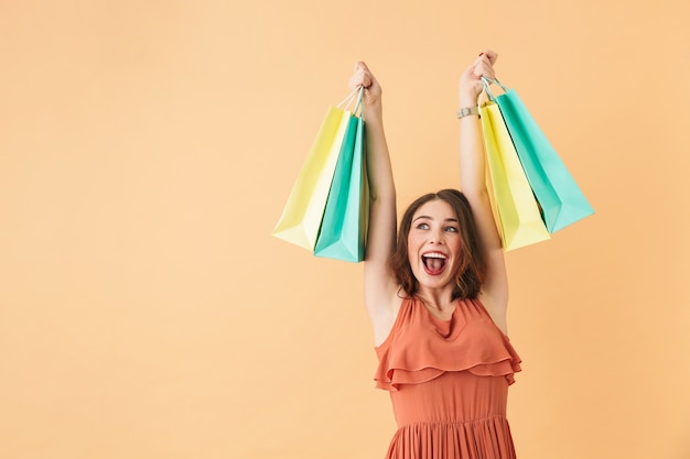 Portrait of excited girl 20s carrying colorful paper shopping bags, while standing isolated 