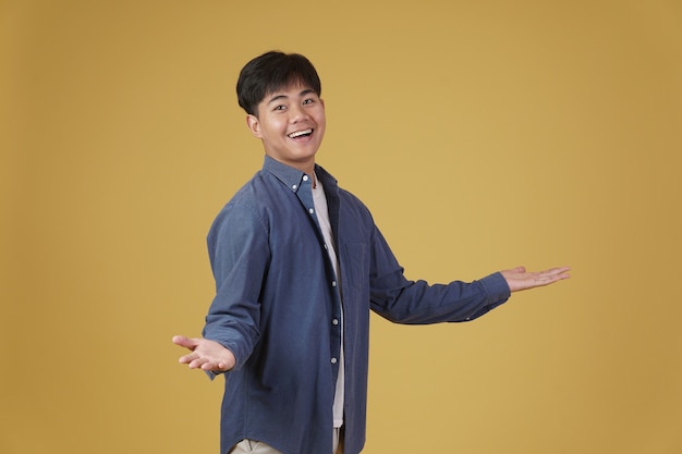 Portrait of excited happy handsome young asian man dressed casually smiling with open hand gesture isolated