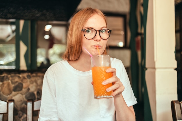 Portrait of excited happy lady drinking healthy orange juice smoothie in city street cafe