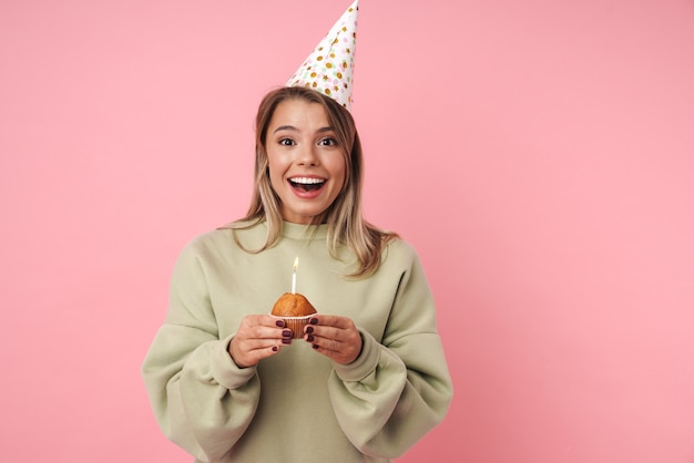 Portrait of excited happy woman in party cone holding cake and looking at camera 