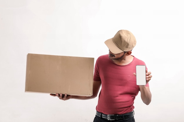 Портрет возбужденного счастливого молодого доставляющего покупки на дом в кепке, стоящей на белом фоне. Глядя камеру, показывающую дисплей мобильного телефона.