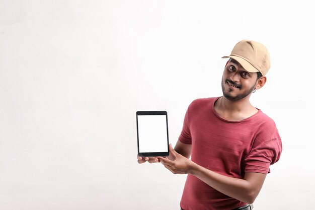 Portrait of a excited happy young delivery man in cap standing over white background. Looking camera showing display of mobile phone.