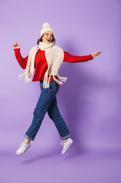 Portrait of an excited happy young woman wearing winter hat isolated over purple wall.