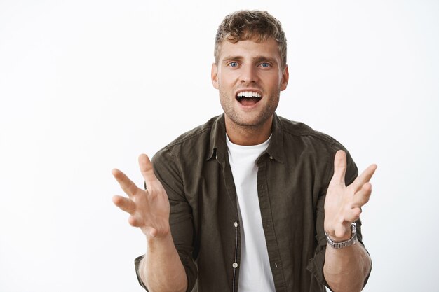 Portrait of excited and impressed happy handsome man gesturing hands over body smiling thrilled and intrigued as telling about awesome product over gray wall