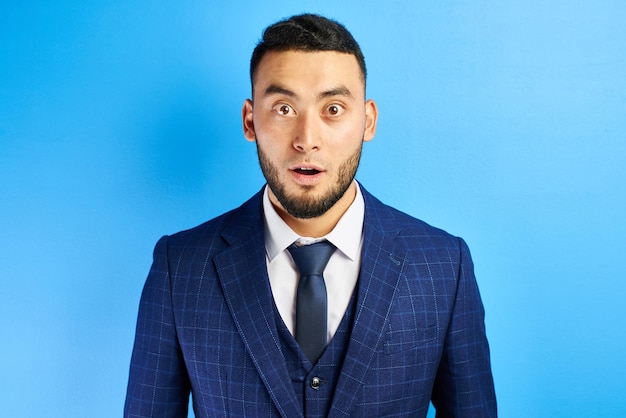 Photo portrait of excited kazakh asian man with surprised open mouth and bulging eyes in a blue suit with a tie isolated in studio