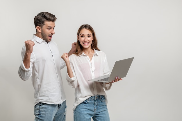 Portrait of excited man and woman screaming and clenching fists like winners holding laptop