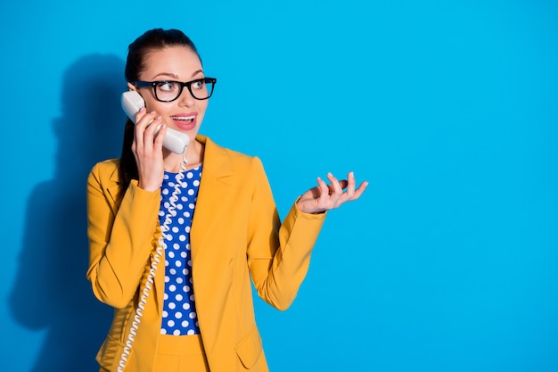Portrait of excited marketer banker assistant girl call telephone friend tell talk say speak business news wear yellow dotted blazer jacket isolated over blue color background
