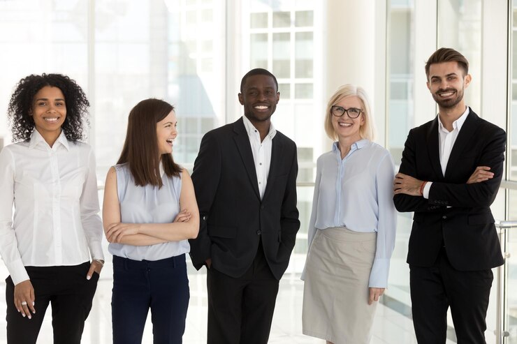 Photo portrait of excited multiethnic work team standing in modern office posing near big windows smiling diverse employees look at camera happy with career success satisfied with company opportunities