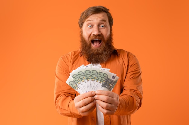 portrait of excited redhaired bearded man shouts holding euro money