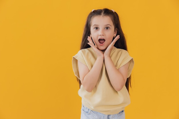 興奮したショックを受けた狂った笑顔の小さな女の子の子どもの肖像画 黄色で隔離された手を握る