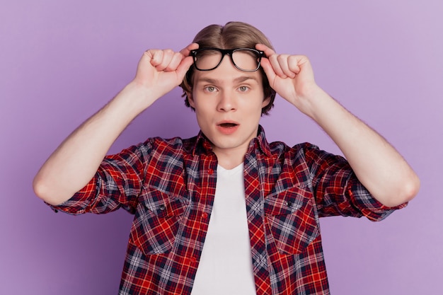 Portrait of excited shocked guy look camera open mouth take off
specs on purple background