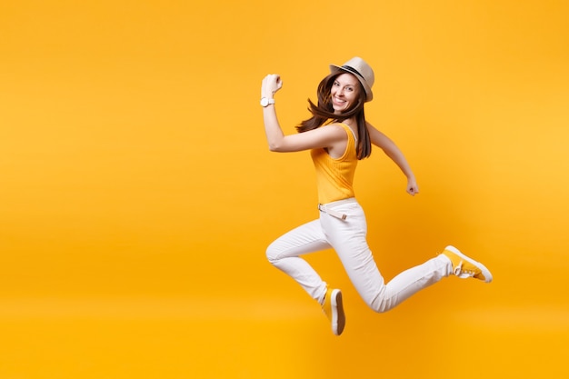 짚으로 여름 모자를 쓴 흥분한 웃고 있는 젊은 행복한 점프 높은 여성의 초상화, 노란색 주황색 배경에 격리된 복사 공간. 사람들은 진실한 감정, 열정적인 라이프스타일 개념입니다. 광고 영역입니다.