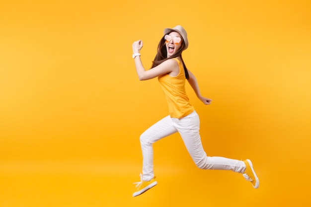 Portrait of excited smiling young jumping high woman in straw summer hat, orange glasses copy space isolated on yellow background. People sincere emotions, passion lifestyle concept. Advertising area.