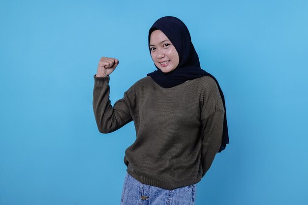 Portrait of an excited woman standing with raised hands and looking at front isolated on a blue wall celebrating succes