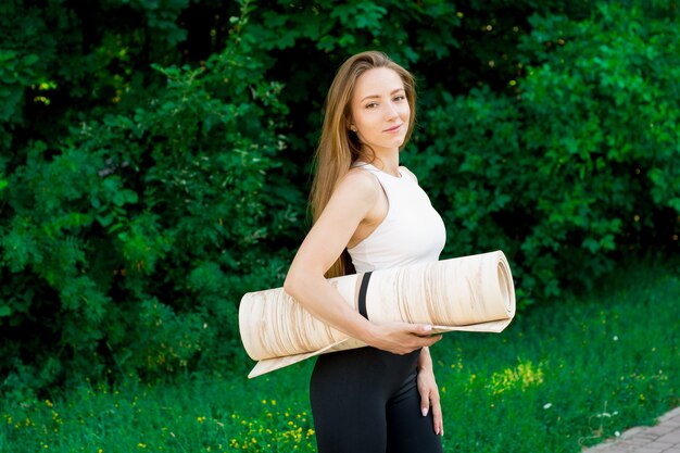 Portrait of excited yoga teacher posing with fitness mat , happy fitness trainer or coach in outdoor sports workout