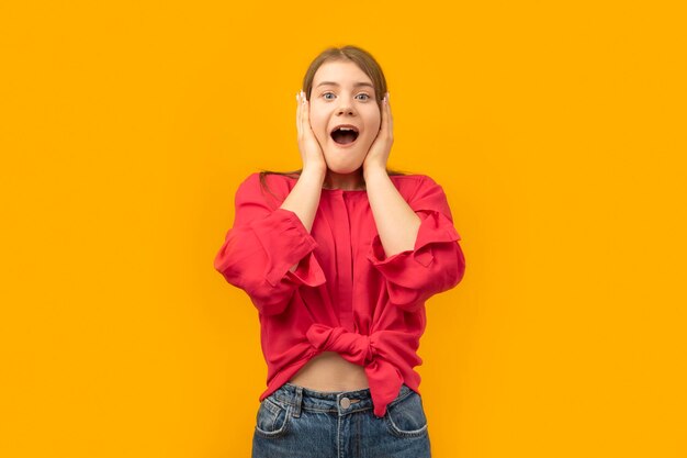 Portrait of excited young girl in youth clothes looking at cameras isolated on the yellow background